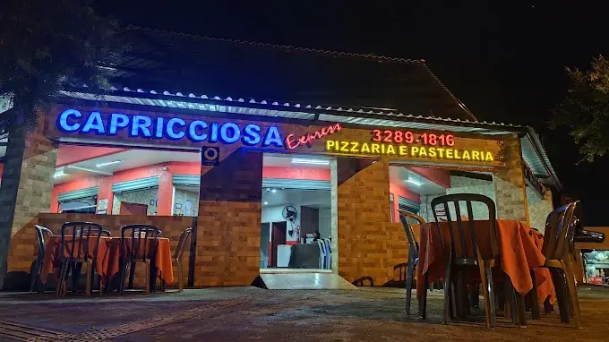Fachada da Capricciosa Express à noite, com o letreiro em neon e mesas na calçada