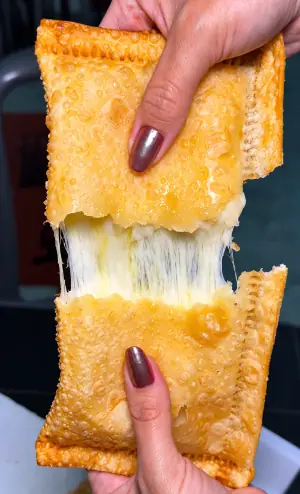 Pastel de queijo aberto ao meio, com o queijo derretido esticando