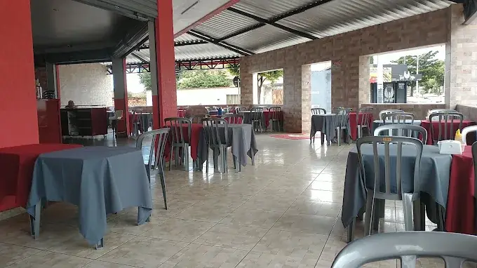 Salão coberto da pizzaria com mesas de toalha vermelha e cinza